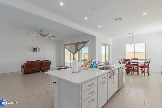 kitchen with white cabinets, pendant lighting, stainless steel dishwasher, a center island with sink, and ceiling fan with notable chandelier