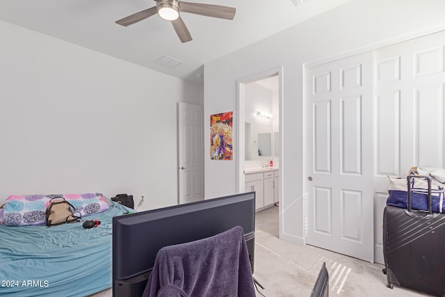 bedroom with a closet, light colored carpet, connected bathroom, and ceiling fan