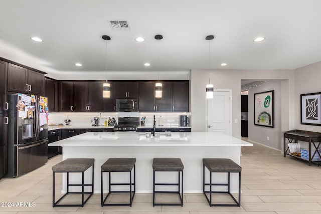 kitchen with appliances with stainless steel finishes, sink, pendant lighting, and an island with sink