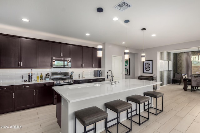 kitchen featuring hanging light fixtures, an island with sink, appliances with stainless steel finishes, and a breakfast bar area