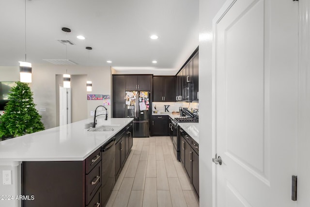 kitchen featuring dark brown cabinets, stainless steel appliances, sink, hanging light fixtures, and an island with sink