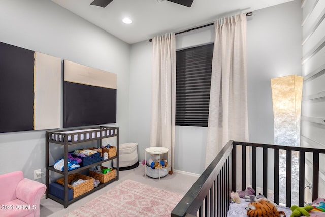 carpeted bedroom with a crib and ceiling fan