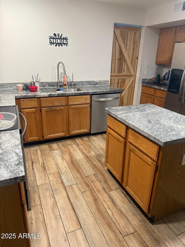 kitchen with a kitchen island, sink, stainless steel appliances, light stone countertops, and light wood-type flooring