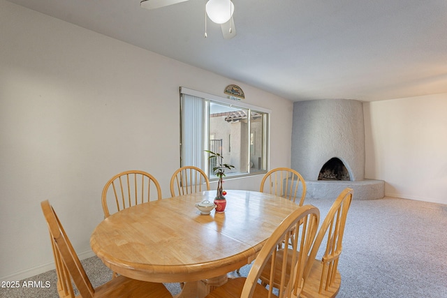 dining space with carpet, a large fireplace, and ceiling fan