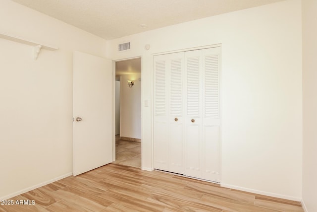 unfurnished bedroom featuring a closet, visible vents, light wood-style flooring, a textured ceiling, and baseboards