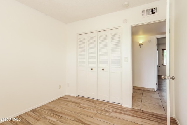 unfurnished bedroom with baseboards, a closet, visible vents, and light wood-style floors