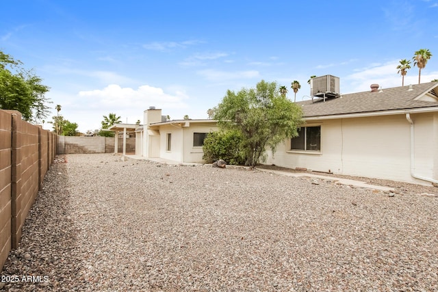 rear view of property featuring a shingled roof, a chimney, a fenced backyard, and central air condition unit