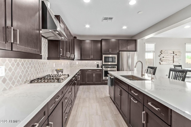 kitchen featuring visible vents, a sink, appliances with stainless steel finishes, wall chimney exhaust hood, and dark brown cabinets