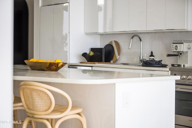 kitchen featuring white cabinetry, a kitchen breakfast bar, white fridge, electric stove, and decorative backsplash