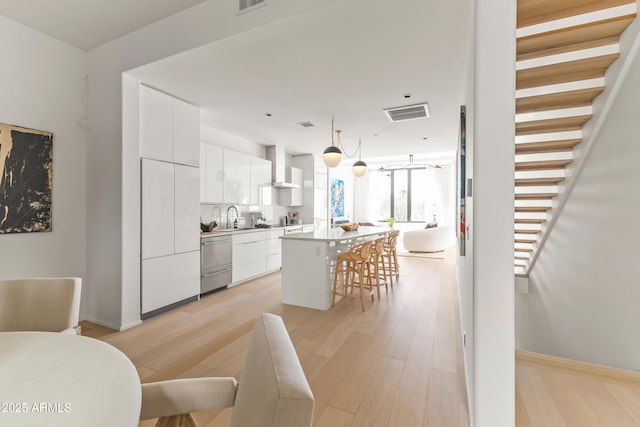 kitchen with a kitchen bar, a center island, white cabinets, pendant lighting, and wall chimney range hood