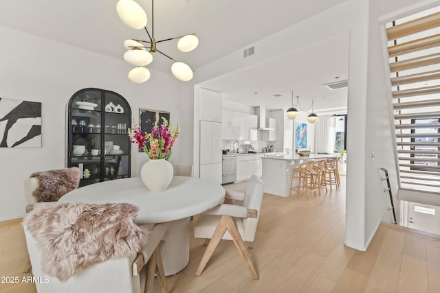 dining space featuring light wood-type flooring, visible vents, and a notable chandelier