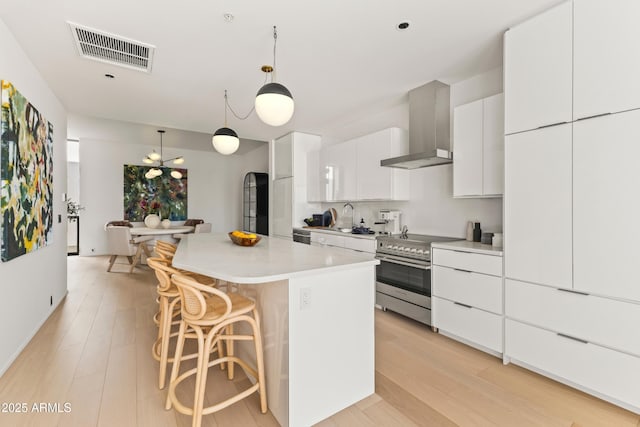 kitchen featuring visible vents, wall chimney exhaust hood, a kitchen island, stainless steel electric range, and a kitchen bar