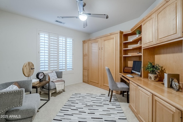 office area with built in desk, light colored carpet, and ceiling fan