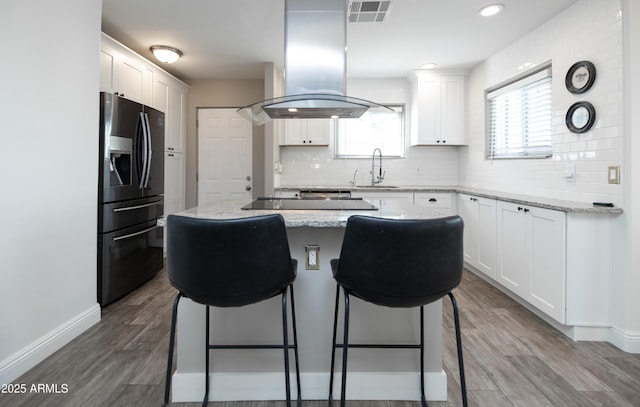 kitchen with white cabinetry, a center island, island range hood, and fridge with ice dispenser