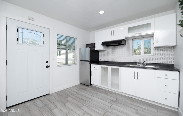 kitchen featuring sink, light wood-type flooring, stainless steel refrigerator, white cabinets, and backsplash