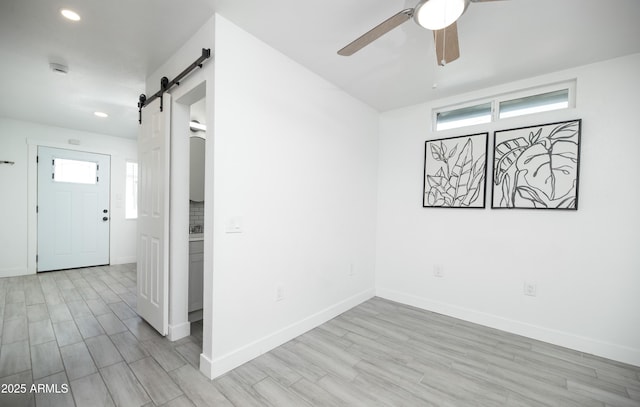 unfurnished room featuring ceiling fan, a barn door, and light wood-type flooring