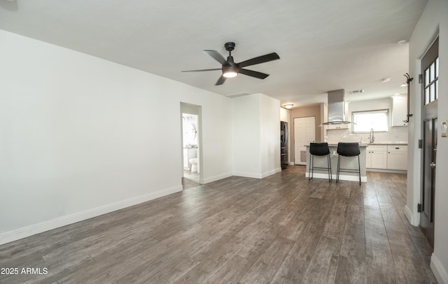 unfurnished living room featuring hardwood / wood-style floors, sink, and ceiling fan