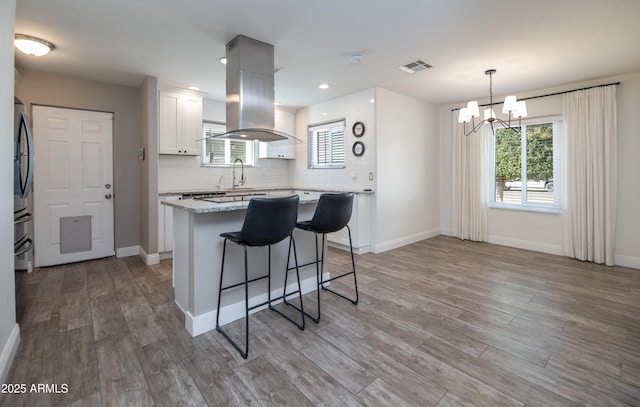 kitchen featuring decorative light fixtures, light wood-type flooring, island exhaust hood, decorative backsplash, and white cabinets