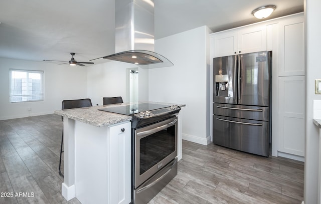 kitchen featuring white cabinetry, appliances with stainless steel finishes, island range hood, and a kitchen breakfast bar