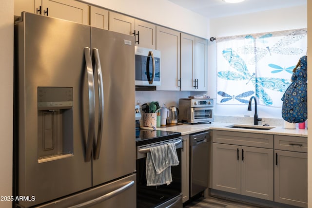 kitchen with light stone counters, gray cabinets, appliances with stainless steel finishes, and a sink