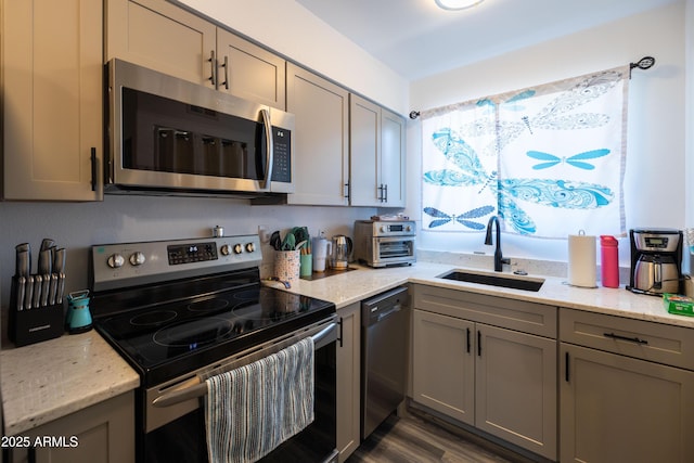 kitchen featuring light stone countertops, gray cabinetry, stainless steel appliances, and a sink