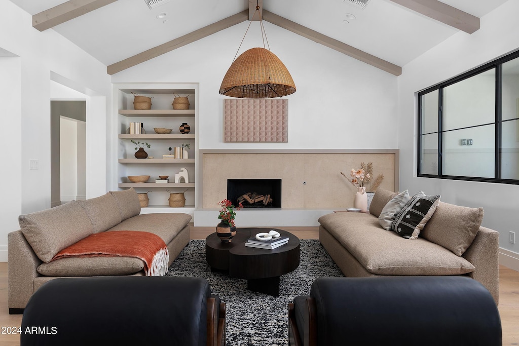 living area featuring built in shelves, visible vents, lofted ceiling with beams, a premium fireplace, and wood finished floors