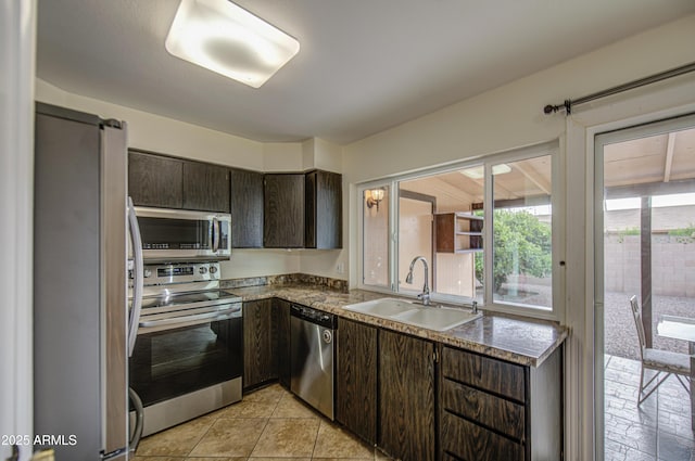 kitchen with dark brown cabinetry, dark countertops, a sink, stainless steel appliances, and light tile patterned floors