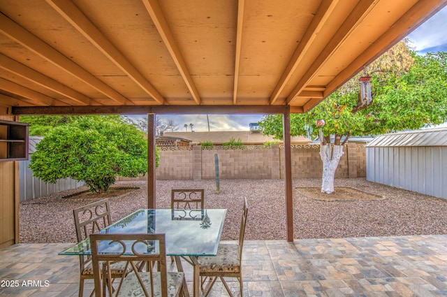 view of patio / terrace featuring a fenced backyard, an outdoor structure, outdoor dining area, and a storage shed
