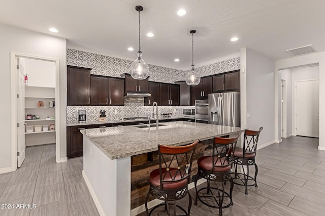 kitchen with light stone countertops, sink, stainless steel refrigerator with ice dispenser, a breakfast bar, and a center island with sink