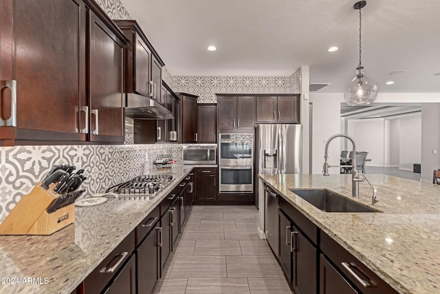 kitchen featuring light stone countertops, appliances with stainless steel finishes, backsplash, sink, and hanging light fixtures