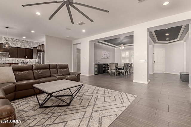 living room with hardwood / wood-style floors, ceiling fan with notable chandelier, a raised ceiling, and crown molding