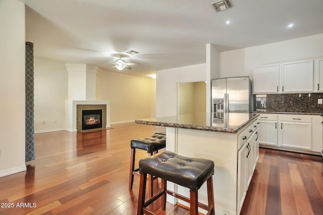 kitchen featuring a kitchen island, white cabinetry, a breakfast bar area, dark stone countertops, and stainless steel refrigerator with ice dispenser