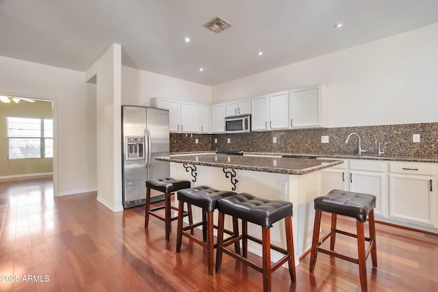 kitchen with sink, dark stone countertops, stainless steel appliances, a center island, and a kitchen bar