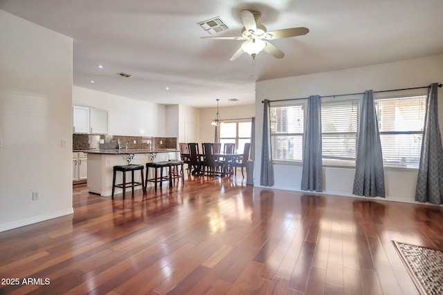 living room featuring ceiling fan with notable chandelier and dark wood-type flooring