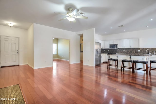 kitchen with appliances with stainless steel finishes, dark hardwood / wood-style floors, tasteful backsplash, white cabinetry, and a breakfast bar area