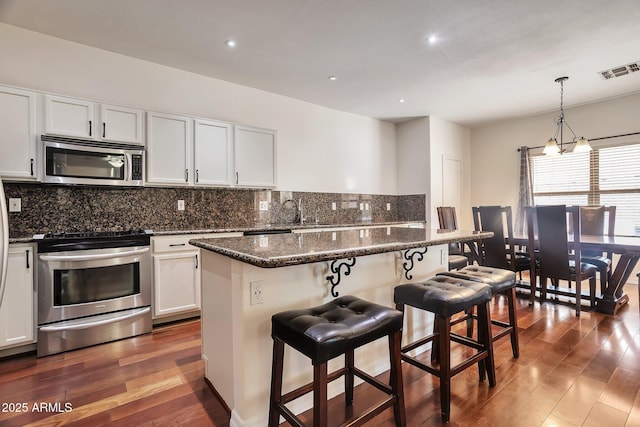 kitchen featuring white cabinetry, appliances with stainless steel finishes, a kitchen island, pendant lighting, and dark stone counters