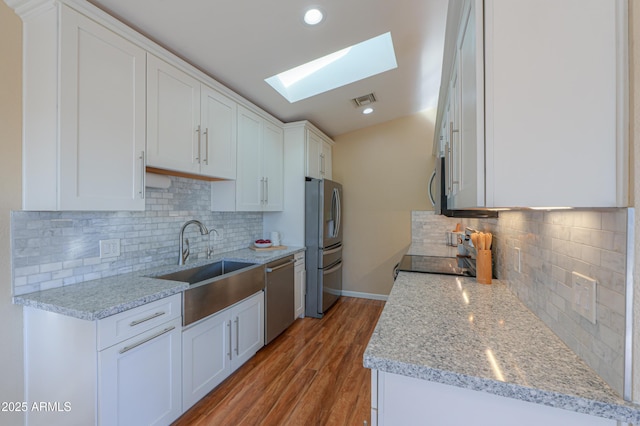 kitchen featuring appliances with stainless steel finishes, a skylight, tasteful backsplash, light stone counters, and white cabinetry