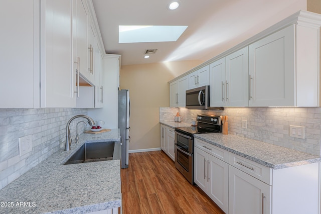 kitchen featuring appliances with stainless steel finishes, a skylight, light stone counters, sink, and white cabinetry