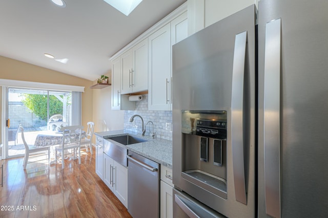 kitchen with white cabinets, lofted ceiling with skylight, appliances with stainless steel finishes, and tasteful backsplash