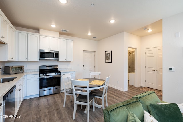 kitchen featuring appliances with stainless steel finishes, dark hardwood / wood-style floors, light stone countertops, and white cabinets