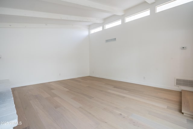 spare room featuring beam ceiling, light hardwood / wood-style floors, and a high ceiling