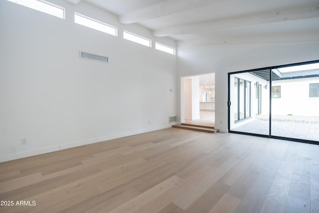 spare room featuring beam ceiling, light hardwood / wood-style floors, and a towering ceiling