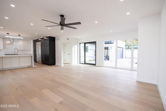 unfurnished living room featuring ceiling fan, sink, and light wood-type flooring