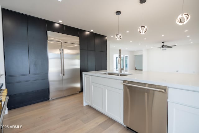 kitchen with stainless steel appliances, sink, light hardwood / wood-style floors, and decorative light fixtures