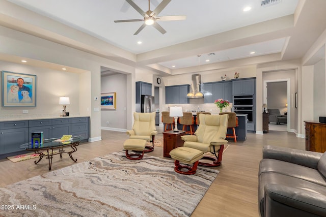 living room with light hardwood / wood-style floors, ceiling fan, and a tray ceiling