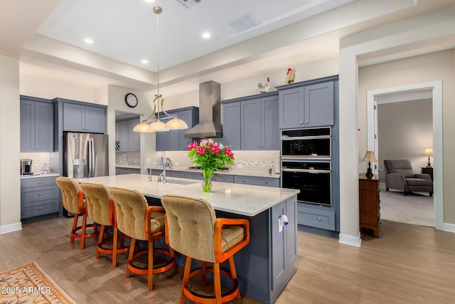 kitchen featuring decorative light fixtures, light stone counters, wall chimney exhaust hood, a breakfast bar area, and a kitchen island with sink