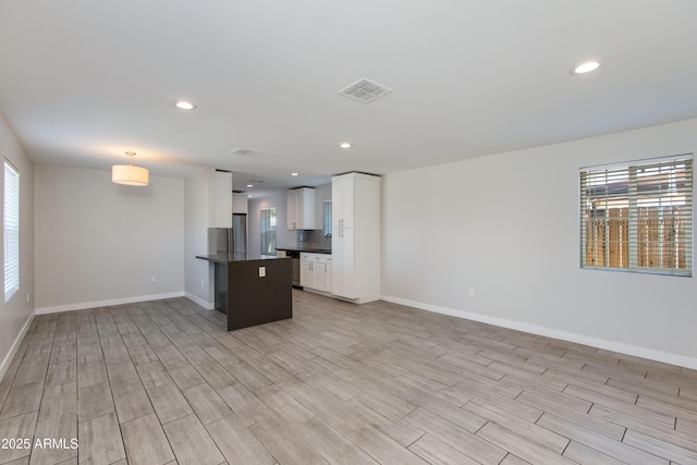 interior space featuring visible vents, light wood-style floors, white cabinetry, dark countertops, and open floor plan