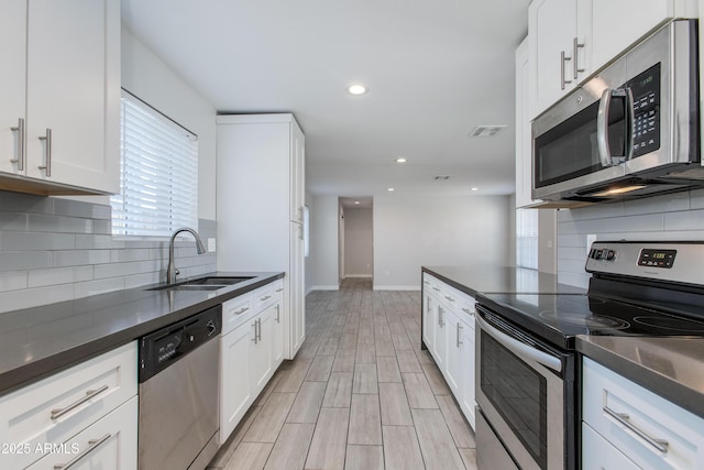 kitchen featuring visible vents, a sink, appliances with stainless steel finishes, white cabinetry, and dark countertops