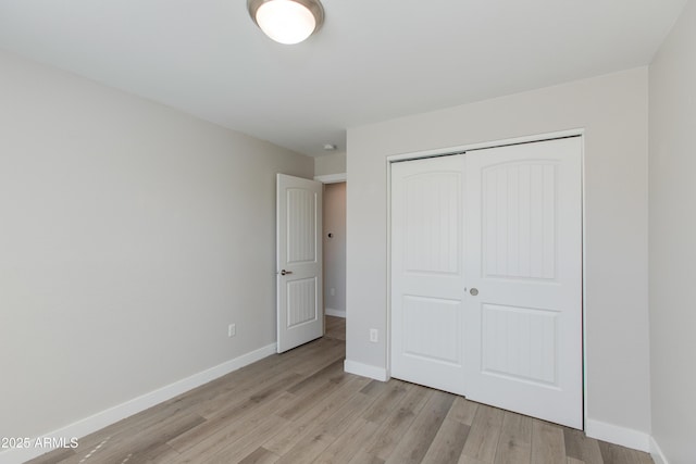 unfurnished bedroom featuring baseboards, light wood-type flooring, and a closet