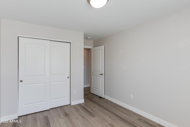 unfurnished bedroom featuring baseboards, light wood-type flooring, and a closet